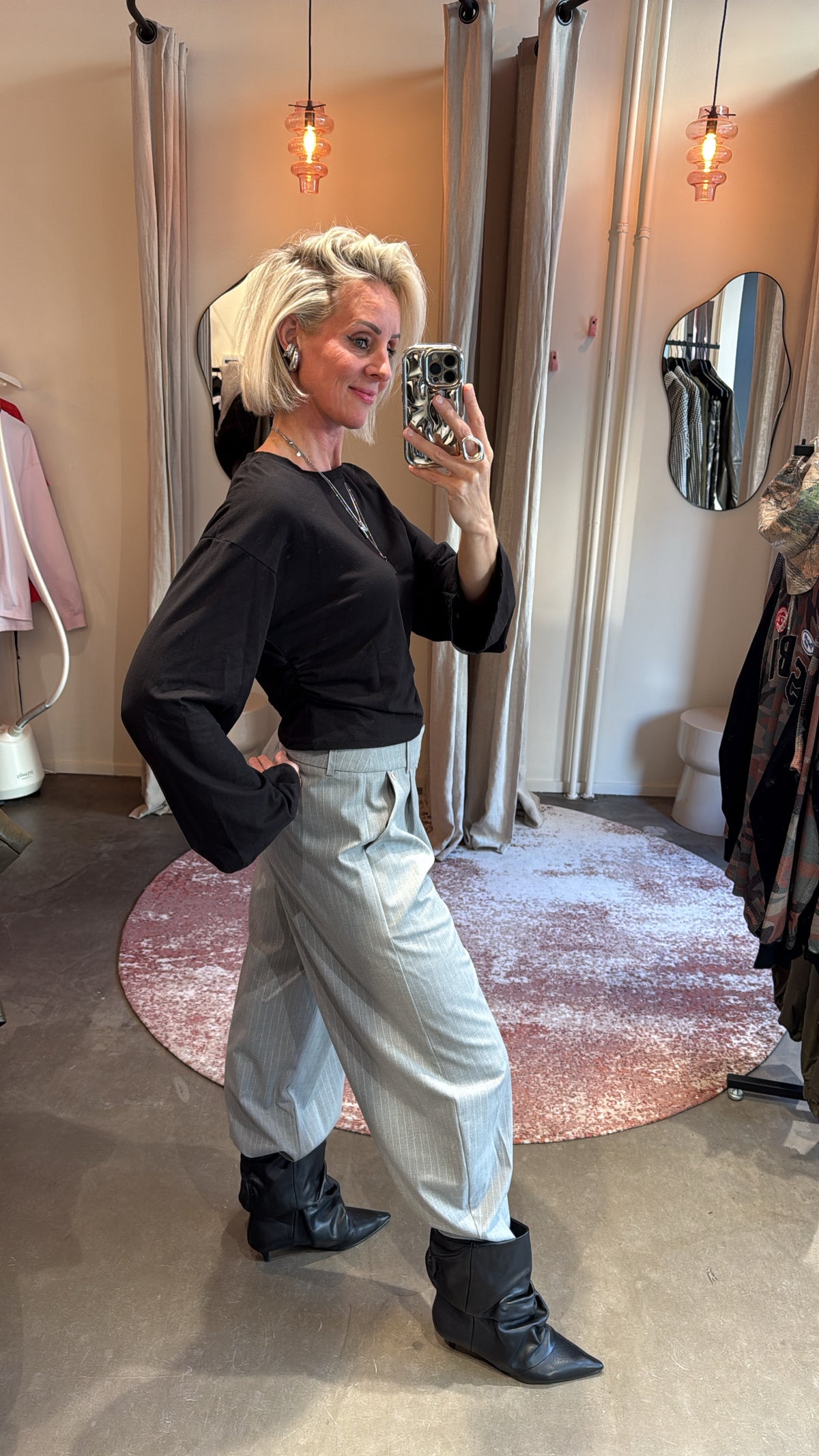 zijaanzicht van model in zwarte longsleeve met wijde mouwen, gecombineerd met grijze pantalon